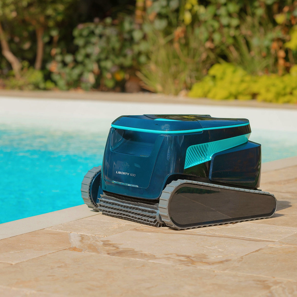 Robot piscina Dolphin Liberty 600i su bordo piscina, design moderno e compatto, vegetazione sullo sfondo.