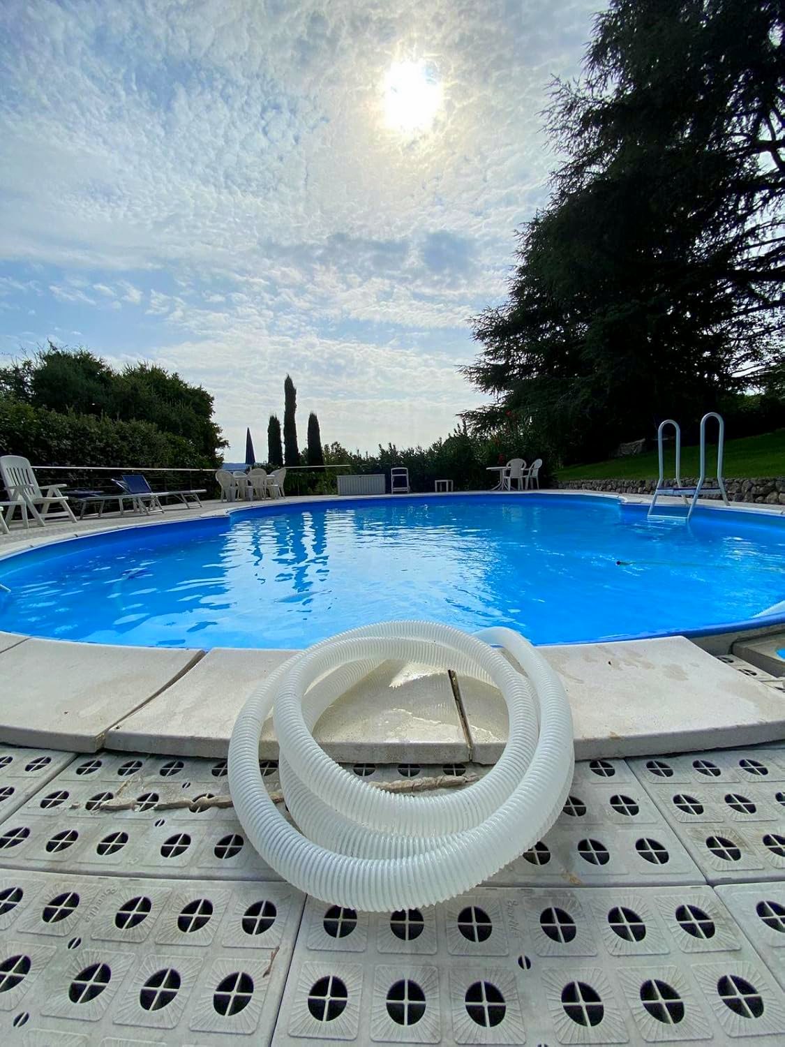 Tubo spiralato piscina galleggiante su bordo piscina, cielo nuvoloso e sole alto.