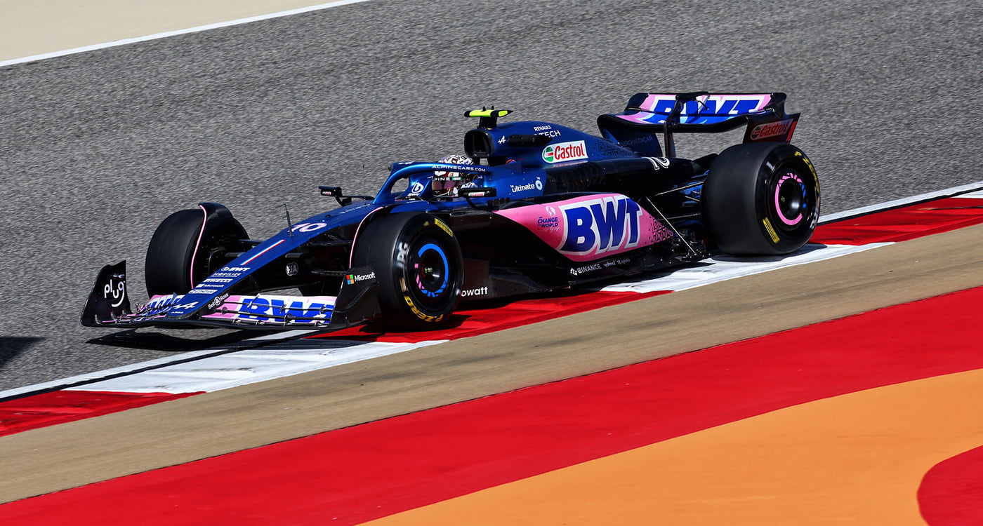 Auto da corsa blu e rosa in pista, curva su asfalto grigio e strisce rosse.