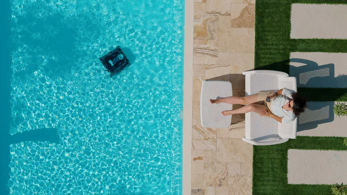 Robot piscina Dolphin Liberty 600i in azione, accanto a una persona su sdraio a bordo piscina.