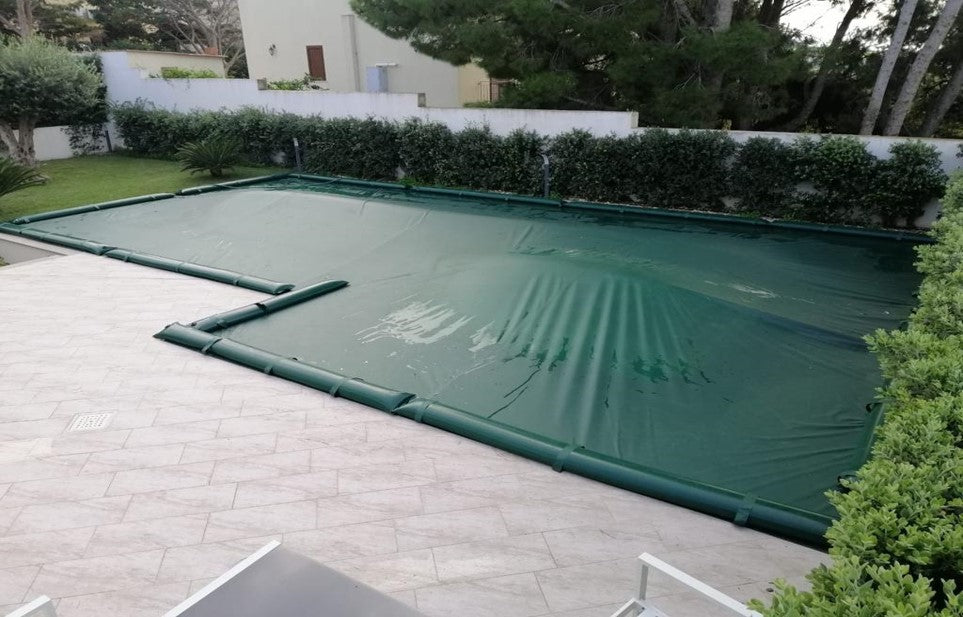 Telo di copertura verde su piscina rettangolare in giardino, senza tubolari perimetrali.
