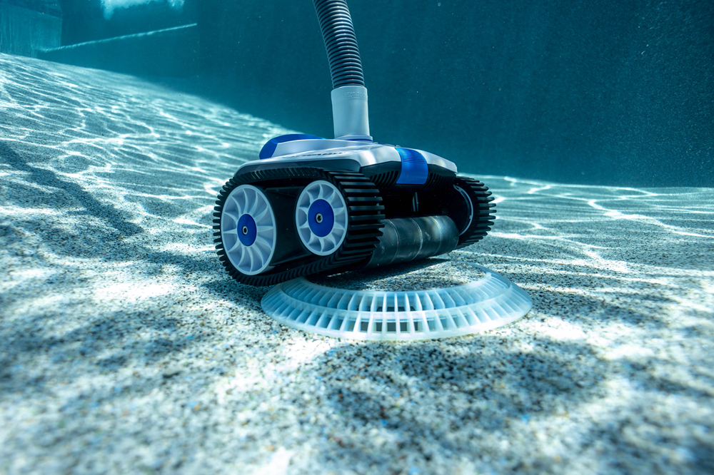 Robot piscina Hayward TracVac in azione sul fondo, con cingoli e tubo idraulico visibili.