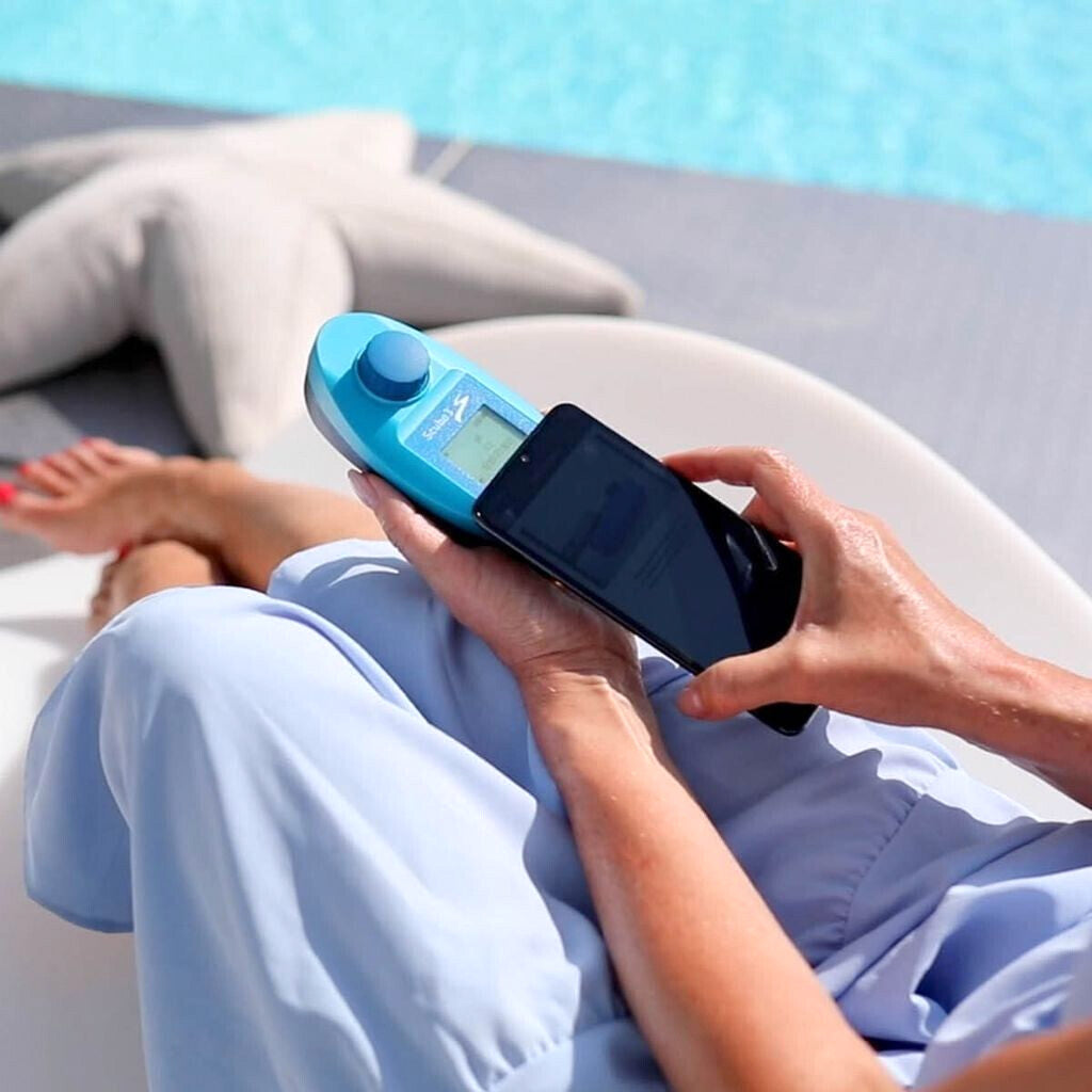 Fotometro Lovibond Scuba 3S tenuto in mano a bordo piscina, accanto a uno smartphone.