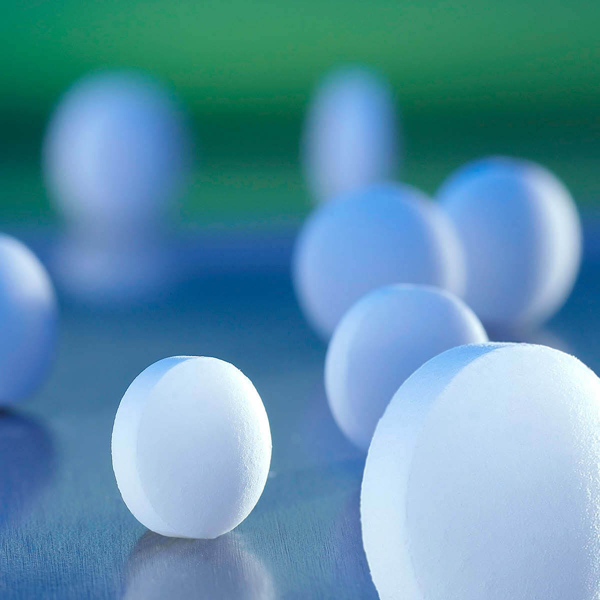 Pastiglie bianche per test PH su superficie blu, sfondo sfocato verde.