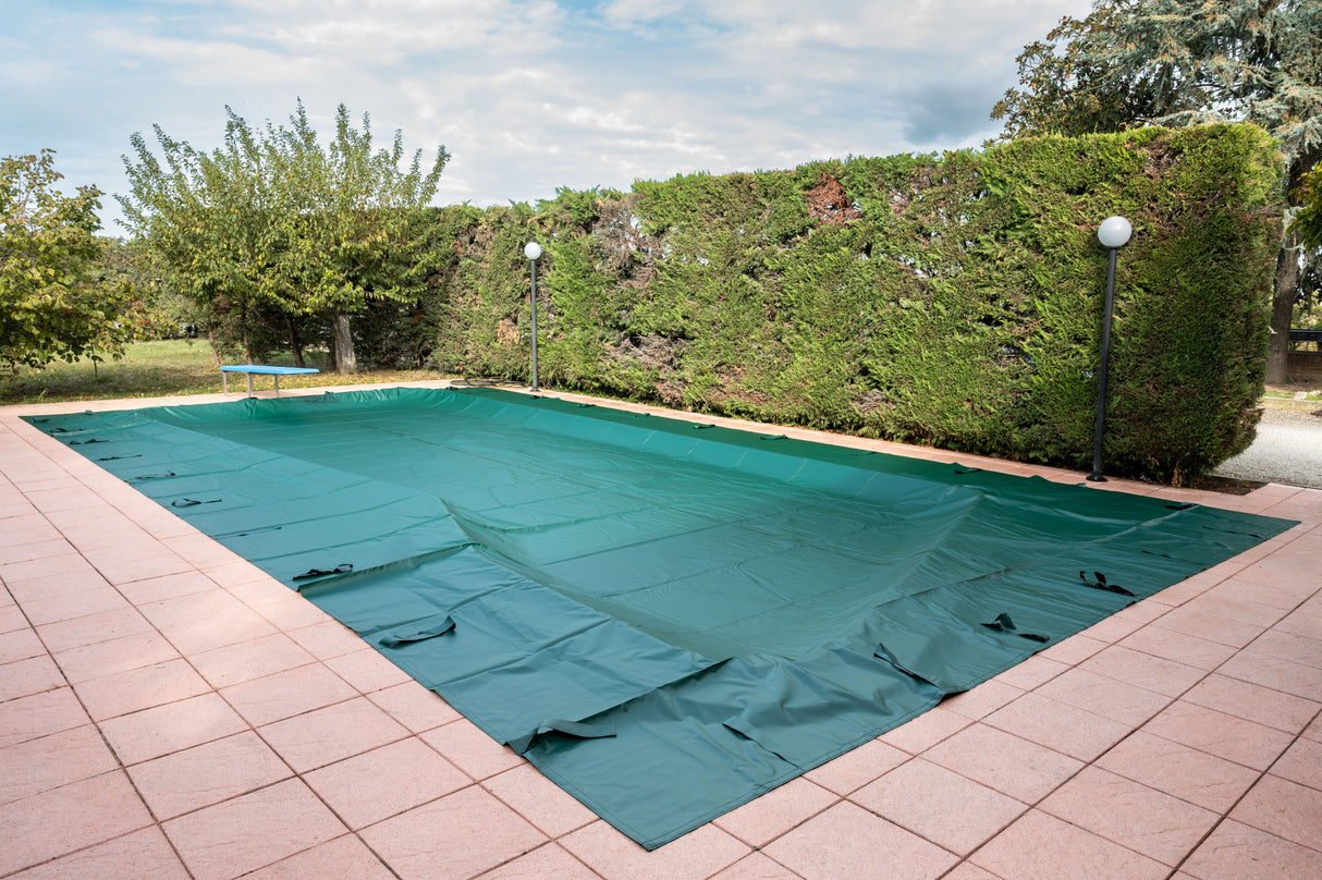 Copertura invernale verde per piscina su pavimento piastrellato, circondata da siepi.