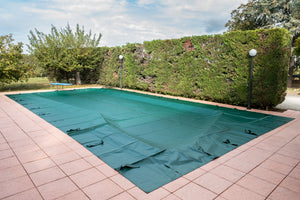 Copertura invernale verde per piscina su pavimento piastrellato, circondata da siepi.