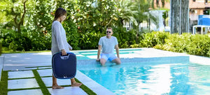 Donna con robot piscina Dolphin Skimmi 300 vicino a una piscina, uomo seduto sul bordo.