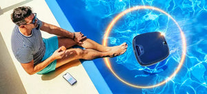 Robot piscina Dolphin Skimmi 300 galleggia in acqua vicino a una persona seduta a bordo piscina.