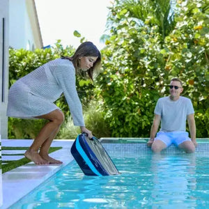 Donna posiziona il robot Dolphin Skimmi 300 a bordo piscina, uomo seduto vicino.