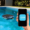 Robot piscina Dolphin Skimmi 300 galleggia in acqua, smartphone con app di controllo visibile.