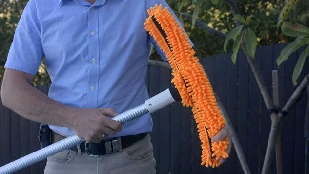 Spazzola in microfibra arancione su manico telescopico per piscina, tenuta da una persona.