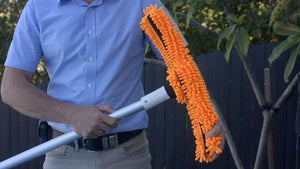 Spazzola in microfibra arancione su manico telescopico per piscina, tenuta da una persona.